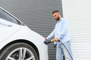 stilvoll Mann Einsätze Stecker in das elektrisch Auto Laden Steckdose foto