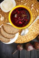 rot traditionell Russisch und ukrainisch Borscht oder Rote Beete Suppe mit sauer Creme, Knoblauch und Aromen im ein Gelb Keramik Tasse auf Korbweide Tischset Hintergrund. foto