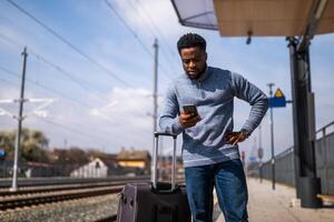 schockiert Mann mit ein Koffer und Handy, Mobiltelefon Telefon Stehen auf ein Eisenbahn Bahnhof. foto