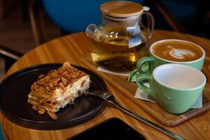 ein Tasse von Kaffee und ein Tasse von Grün Tee und Kuchen auf ein hölzern Tabelle im ein Cafe. foto