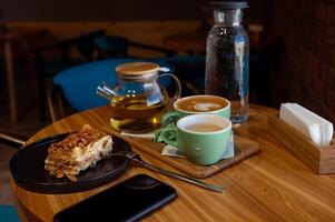 ein Tasse von Kaffee und ein Tasse von Grün Tee und Kuchen auf ein hölzern Tabelle im ein Cafe. foto