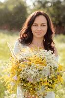 Porträt von ein dunkelhaarig Mädchen mit ein groß Strauß von Wildblumen. foto