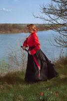 ein Frau mit kurz rot Haar im schwarz und rot Hanfu und ein Katana auf das Hintergrund von ein Fluss im Frühling foto