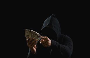 Porträt Mörder Hacker Mafia Gangster Spion Mann eine Person im schwarz Kapuzenpullover Stehen aussehen Hand halten Geld Dollar erhalten von Raub Drohung Verbrechen Attacke Opfer Menschen Nacht dunkel Hintergrund Kopieren Raum foto