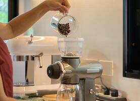 Frau Gießen Kaffee Bohnen in das Kaffee Schleifer Maschine im das Küche beim Zuhause foto