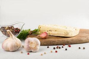 Soja Vegetarier Käse auf ein Planke. in der Nähe von Knoblauch, Pfefferkörner und ein Bündel von Grüns. gesund Lebensmittel. Vegetarismus foto
