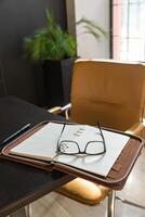 Büro Arbeitsplatz. Gelb Stuhl und schwarz Schreibtisch im Zuhause Büro. das Schreibtisch hält ein öffnen Veranstalter, Stift und Brille. foto