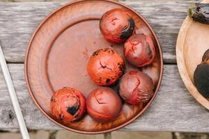 gebacken Tomaten auf ein Lehm Platte. bunt ganze Tomaten mit Skins geknackt auf das Feuer. foto