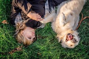 Schöne kaukasische Frau, die mit ihrem goldenen Labrador Retriever-Hund in einem Park im Sonnenuntergang im Gras liegt? foto