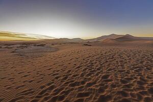 Panorama- Bild von das rot Dünen von das namib Wüste mit Fußabdrücke im das Sand gegen Blau Himmel foto