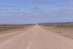 Panorama- Bild Über ein Kies Straße durch das Wüste mögen Steppe im Süd- Namibia unter ein Blau Himmel foto