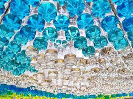 niedrig Winkel Aussicht von dekorativ Overhead Decke Vorhang gemacht von recycelt Plastik Trinken Flaschen gefüllt mit bunt Wasser und schön Licht Reflexionen auf Oberfläche, Konzept von DIY Zuhause Dekor foto