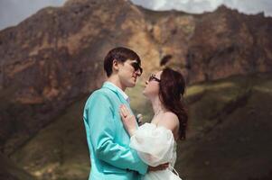 ein jung Mann und seine Ehefrau Stand im ein Umarmung hoch im das Berge gegen das Hintergrund von Epos Felsen auf ein sonnig Tag. Jungvermählten Hochzeit Paar im das Berge foto
