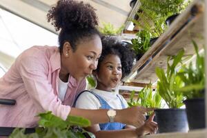 afrikanisch Mutter und Tochter ist wählen tropisch Farn und Zier Pflanzen von das lokal Garten Center Kindergarten während Sommer- zum Wochenende Gartenarbeit und draussen foto