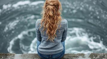 ein Frau sitzt auf ein Leiste, Blick beim das Wasser unten foto