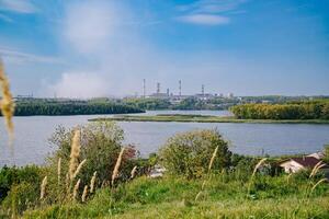 Fluss Teilen Grün Dorf und Fabrik mit groß emittieren Schornsteine foto