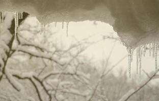 Mehrere Eiszapfen befinden sich über dem verschwommenen Winterblick aus dem Fenster foto