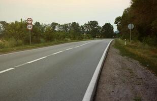 leeren Asphalt Straße und Blumen- Feld von anders Gras und Blumen im Abend Zeit foto