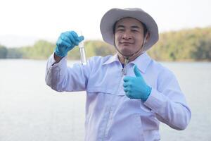 asiatischer mann umweltforscher hält röhrchen mit probewasser zur inspektion aus dem see. Konzept, Erkundung, Analyse der Wasserqualität aus natürlichen Quellen. Ökologische Feldforschung. foto