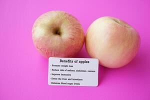 zwei Äpfel mit Etikett von Text Leistungen von Äpfel. Rosa Hintergrund. Konzept, Apfel Früchte mit gut Qualifikation zum Gesundheit. Foto zum Bildung. Lehren Hilfe. gesund Essen, Obst Lektion.