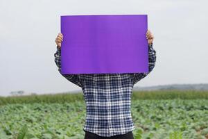 Farmer halt leer violett Papier Poster beim Garten Hintergrund. Konzept, Landwirtschaft Beruf. Kopieren Raum zum Hinzufügen Text oder Werbung. Protest. Bekanntmachung. foto