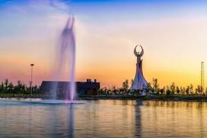Usbekistan, Taschkent - - April 25, 2023 das Gebiet von das Park Neu Usbekistan mit Monument von Unabhängigkeit im das bilden von ein Stele mit ein Humo Vogel, Teich und Brunnen beim Dämmerung. foto