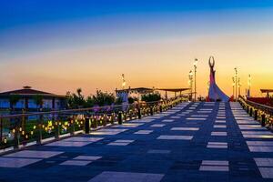 Usbekistan, Taschkent - - April 25, 2023 das Gebiet von das Park Neu Usbekistan mit Monument von Unabhängigkeit im das bilden von ein Stele mit ein Humo Vogel beim Dämmerung. Aussicht von ein Brücke. foto