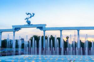 Denkmal und Reihen von Brunnen beleuchtet durch Sonnenlicht beim Sonnenuntergang oder Sonnenaufgang im das Unabhängigkeit Platz beim Sommer, Taschkent. foto