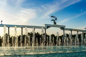 Denkmal und Reihen von Brunnen beleuchtet durch Sonnenlicht beim Sonnenuntergang oder Sonnenaufgang im das Unabhängigkeit Platz beim Sommer, Taschkent. foto