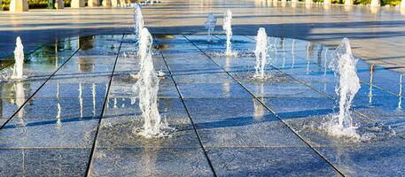 Streams von planschen klein Brunnen auf nass Pflasterung Platten, beleuchtet durch das Sonne im ein Sommer. foto