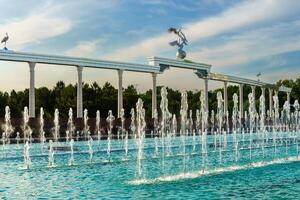 Denkmal und Reihen von Brunnen beleuchtet durch Sonnenlicht beim Sonnenuntergang oder Sonnenaufgang im das Unabhängigkeit Platz beim Sommer, Taschkent. foto