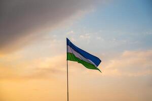 Flagge von Usbekistan winken auf ein Sonnenuntergang oder Sonnenaufgang dramatisch Himmel Hintergrund. foto