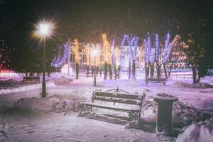 Winter Park beim Nacht mit Weihnachten Dekorationen, glühend Laternen, Pflaster bedeckt mit Schnee und Bäume. Jahrgang Film ästhetisch. foto