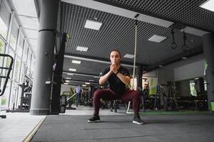 Seite Aussicht Porträt von ein jung Frau tun Kniebeugen beim Fitness Fitnessstudio. foto