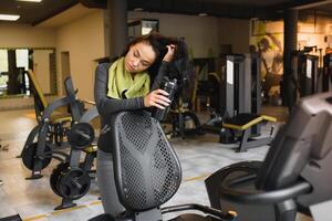 jung Frau Trinken Wasser und nehmen ein brechen nach trainieren im Fitnessstudio foto