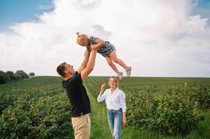 das Tochter umarmen Eltern auf Natur. Mutter, Papa und Mädchen Kleinkind, gehen im das Gras. glücklich jung Familie Ausgaben Zeit zusammen, außen, auf Urlaub, draußen. das Konzept von Familie Urlaub foto