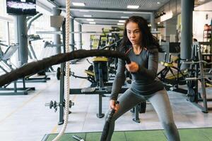 ziemlich spanisch jung Frau tun etwas Crossfit Übungen mit ein Seil beim ein Fitnessstudio. foto