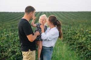 das Tochter umarmen Eltern auf Natur. Mutter, Papa und Mädchen Kleinkind, gehen im das Gras. glücklich jung Familie Ausgaben Zeit zusammen, außen, auf Urlaub, draußen. das Konzept von Familie Urlaub foto