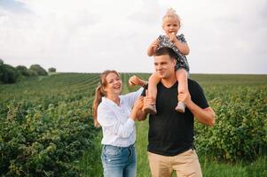 das Tochter umarmen Eltern auf Natur. Mutter, Papa und Mädchen Kleinkind, gehen im das Gras. glücklich jung Familie Ausgaben Zeit zusammen, außen, auf Urlaub, draußen. das Konzept von Familie Urlaub foto