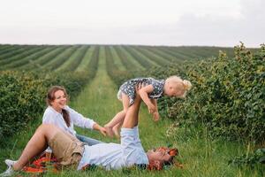 das Tochter umarmen Eltern auf Natur. Mutter, Papa und Mädchen Kleinkind, gehen im das Gras. glücklich jung Familie Ausgaben Zeit zusammen, außen, auf Urlaub, draußen. das Konzept von Familie Urlaub foto