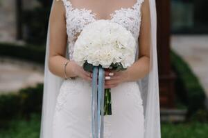 Braut steht im ein Weiß Hochzeit Kleid mit ein Strauß von Blumen foto