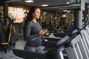 jung passen Frau Laufen auf Laufband Hören zu Musik- über Kopfhörer beim Fitnessstudio. Konzept von gesund Lebensstil foto