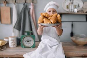 jung Junge süß auf das Küche Koch Koch im Weiß Uniform und Hut in der Nähe von Tisch. hausgemacht Lebkuchen. das Junge gekocht das Schokolade Kekse. foto