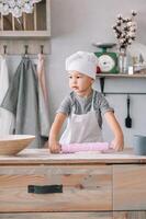 jung Junge süß auf das Küche Koch Koch im Weiß Uniform und Hut in der Nähe von Tisch. hausgemacht Lebkuchen. das Junge gekocht das Schokolade Kekse foto