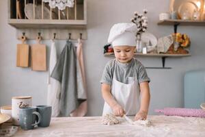 jung Junge süß auf das Küche Koch Koch im Weiß Uniform und Hut in der Nähe von Tisch. hausgemacht Lebkuchen. das Junge gekocht das Schokolade Kekse. foto