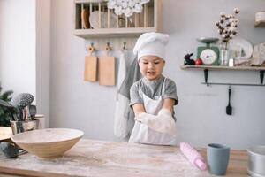 jung Junge süß auf das Küche Koch Koch im Weiß Uniform und Hut in der Nähe von Tisch. hausgemacht Lebkuchen. das Junge gekocht das Schokolade Kekse. foto