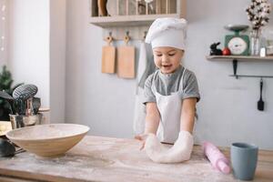 jung Junge süß auf das Küche Koch Koch im Weiß Uniform und Hut in der Nähe von Tisch. hausgemacht Lebkuchen. das Junge gekocht das Schokolade Kekse. foto