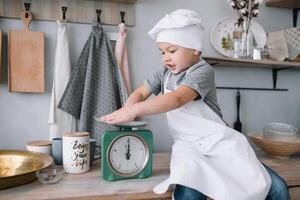 jung Junge süß auf das Küche Koch Koch im Weiß Uniform und Hut in der Nähe von Tisch. hausgemacht Lebkuchen. das Junge gekocht das Schokolade Kekse. foto