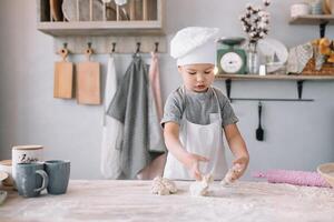 jung Junge süß auf das Küche Koch Koch im Weiß Uniform und Hut in der Nähe von Tisch. hausgemacht Lebkuchen. das Junge gekocht das Schokolade Kekse. foto