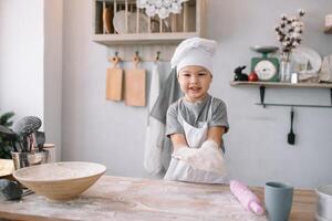 jung Junge süß auf das Küche Koch Koch im Weiß Uniform und Hut in der Nähe von Tisch. hausgemacht Lebkuchen. das Junge gekocht das Schokolade Kekse. foto